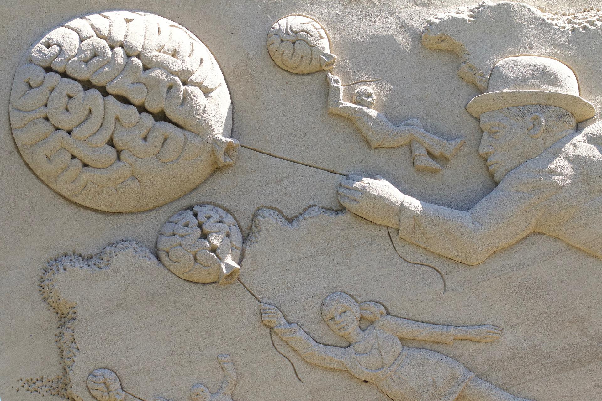 sculpture sur sable de personnes tenant un ballon en forme de cerveau